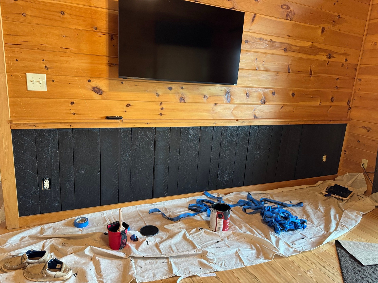 Accent wall painting in progress with drop cloths, blue tape, and paint can in a North Georgia cabin