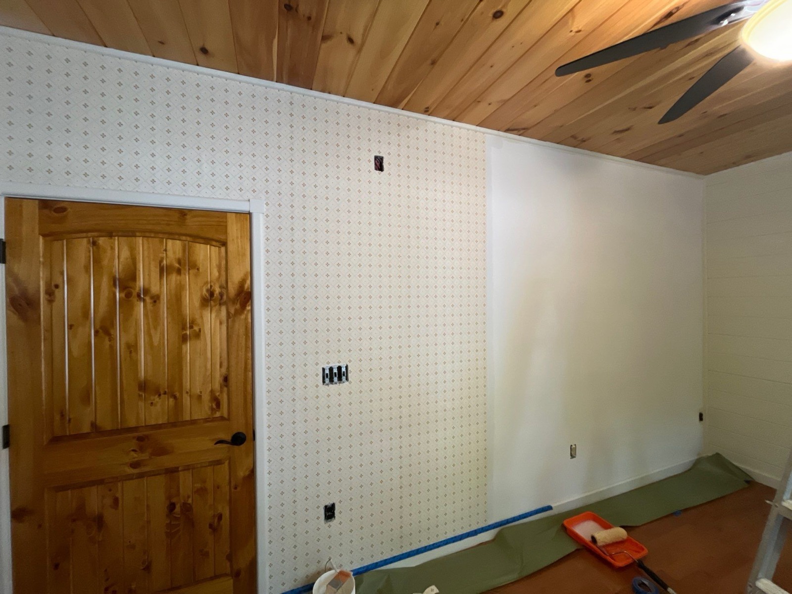 Small-print wallpaper going up on a bedroom wall under a knotty pine ceiling in a North Georgia cabin